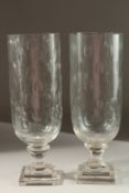 A PAIR OF GLASS STORM LAMPS with circles, on square bases. 35cms high.