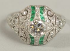 A PLATINUM EMERALD AND DIAMOND DRESS RING with ornate beaded setting. Centre diamond 0.57ct.