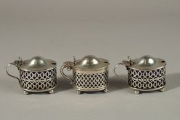 THREE PIERCED OVAL SILVER MUSTARD POTS with sapphire blue liners. Birmingham 1897 and 1904. 4ozs.