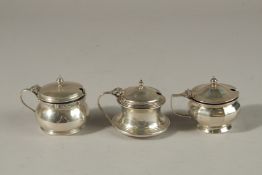 THREE VARIOUS SILVER CIRCULAR PLAIN MUSTARD POTS with sapphire blue liners. Birmingham 1930 and