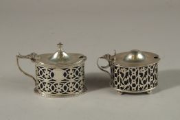 TWO PIERCED OVAL SILVER MUSTARD POTS with sapphire blue liners. Birmingham 1902 and Chester 1903.