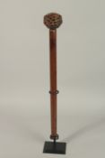 A CARVED WOOD CLUB, the handle as an oval pierced ball. 64cms high, on a metal stand.