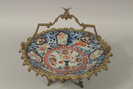 A JAPANESE IMARI PORCELAIN GILDED BRONZE MOUNTED PALETTE DISH, with overarching handle and raised on