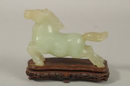 A CHINESE CARVED JADE HORSE, on a pierced wooden stand, 13cm long.