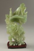 A CHINESE CARVED JADE GROUP ON HARDWOOD STAND, carved with a peacock elevated on a large floral