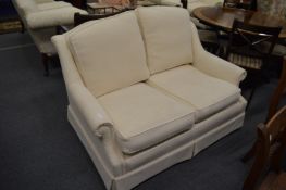 A small cream upholstered two seater settee.