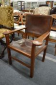An Arts and Crafts walnut framed armchair with leather upholstered back and seat.