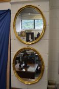 A pair of gilt wood oval mirrors and a similar smaller mirror.