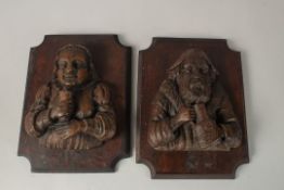 A PAIR OF GERMAN CARVED WOOD PLAQUES, a man and a woman holding wine cups. 35cms x 24cms.
