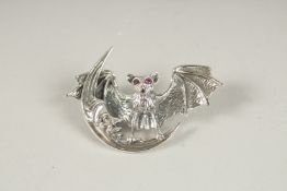 A SILVER RUBY EYE BAT BROOCH.