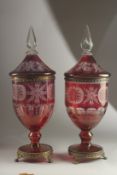 A LARGE PAIR OF BOHEMIAN RUBY TINTED URNS AND COVERS on metal bases with claw feet. 54cms high,