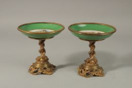 A GOOD PAIR OF SEVRES APPLE GREEN PORCELAIN CIRCULAR TAZZAS painted with cupids, the ormolu bases