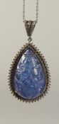 A LARGE PENDANT IN WHITE METAL set with a large pear shaped carved tanzanite surrounded by a