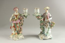 A PAIR OF DERBY FIGURE CANDLESTICKS, as a woman and man, encrusted with flowers, each with a