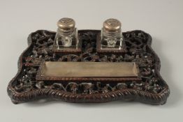 A CHINESE CARVED OPENWORKED HARDWOOD DESK STAND with two glass inkwells and brush rest, 31cm x