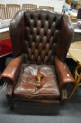 A Georgian design brown leather button upholstered wing armchair.