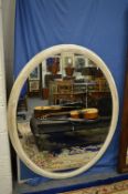 A large oval mirror with distressed white painted frame.