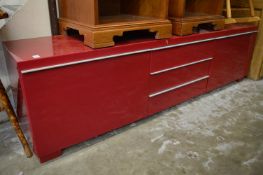 A long low red lacquer storage unit.
