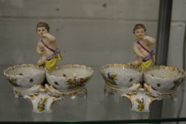 A pair of Continental porcelain double salts mounted with a cherub, each painted with exotic birds