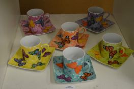 A colourful set of six coffee cans and saucers decorated with butterflies.