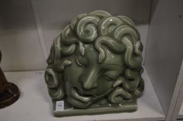 In the manner of Goldscheider, a stylised green glazed pottery mask of Medusa.