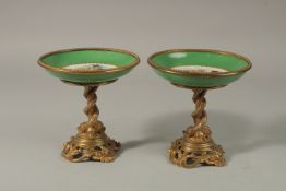 A GOOD PAIR OF SEVRES APPLE GREEN PORCELAIN CIRCULAR TAZZAS painted with cupids, the ormolu bases