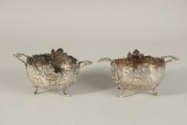 A PAIR OF DUTCH SILVER TWO HANDLED OVAL BOWLS repousse with cupids and scrolls, supported on four