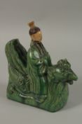 A CHINESE GREEN AND YELLOW GLAZED POTTERY FIGURAL ROOF TILE, formed as a man on a mythical bird