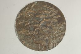 AN ENGRAVED AND CHASED METAL CIRCULAR PLAQUE, depicting cranes beside a tree, 13.5cm diameter.