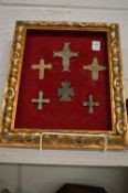 A collection of small cast bronze crosses, mounted and framed.