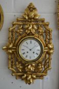 An eight day circular wall clock housed within an ornate carved and gilded frame depicting fruit and
