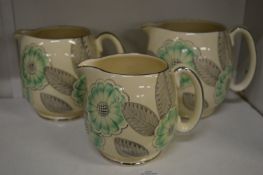 A graduated set of three Grays Pottery jugs decorated with flowers and leaves in green, grey and