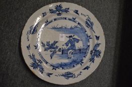 An 18th century tin glazed blue and white charger decorated with a Chinese man standing by a fence.
