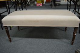 A large upholstered stool with turned legs.