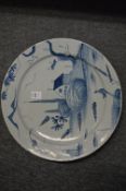 An 18th century tin glazed blue and white charger decorated with a house, trees and a boat.