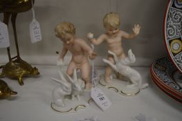 A pair of Continental porcelain figures of young boys playing with rabbits and dogs.