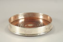 A LARGE SILVER CIRCULAR WINE COASTER with wooden base. 8ins diameter.