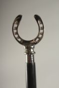 A WOODEN WALKING STICK WITH A HORSESHOE HANDLE.