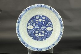 A CHINESE BLUE AND WHITE CARVED FLORAL CHARGER. 44cms diameter.