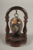 A BLUE JOHN EGG, suspended on a wooden stand. 12cms high.