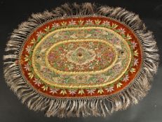 AN INDIAN EMBROIDERED OVAL TEXTILE WITH VARIOUS INSET STONES.