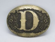 An Award Design Medals Inc belt buckle with D design upon.