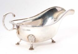 A George V silver sauce boat of typical form with applied decorative rim, flying scroll handle and