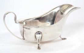 A hallmarked silver sauce boat of typical form having a card cut rim, plain scroll handle and