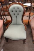 A Victorian mahogany framed nursing chair with buttoned upholstery and scrolled front legs with