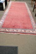 A large 20th Century Middle Eastern wool floor rug decorated with a predominately red central panel,