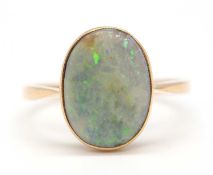 An opal ring, the oval opal cabochon in collet mount with open back and plain band stamped 18ct,