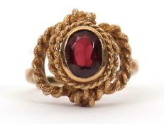 A 9ct garnet ring, the oval faceted garnet in a rubover mount with rope twist border and looped