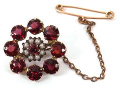 A garnet brooch, set to centre with a small round garnet surrounded by faux pearls and a further