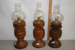 A set of three hardwood candlesticks with glass shades